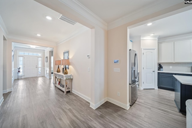 foyer featuring light wood-style flooring, visible vents, and ornamental molding