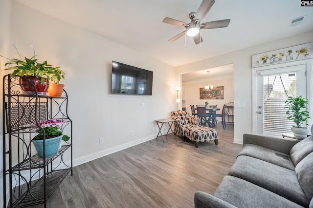 living area with visible vents, baseboards, wood finished floors, and ceiling fan with notable chandelier