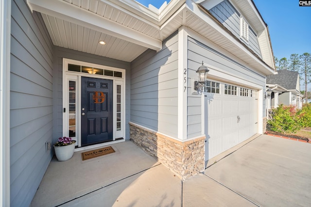 doorway to property featuring a garage, stone siding, and driveway