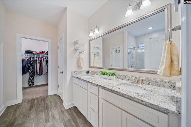 bathroom featuring wood finished floors, double vanity, a stall shower, a sink, and a walk in closet