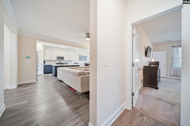 hallway featuring wood finished floors, baseboards, and ornamental molding