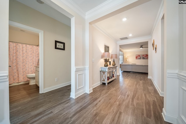 hall with visible vents, wood finished floors, baseboards, and ornamental molding