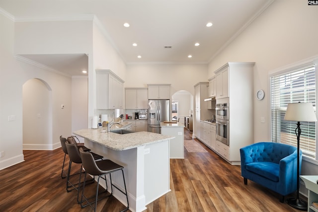 kitchen featuring a sink, a kitchen island, tasteful backsplash, stainless steel appliances, and arched walkways