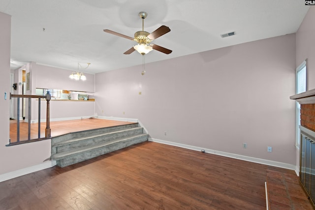 unfurnished living room featuring visible vents, ceiling fan with notable chandelier, wood finished floors, a fireplace, and baseboards