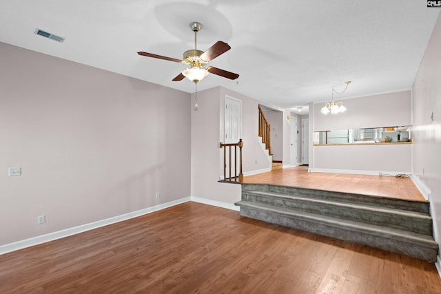 unfurnished living room with stairway, wood finished floors, visible vents, baseboards, and ceiling fan with notable chandelier