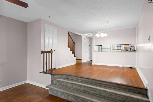 stairway featuring a notable chandelier, wood finished floors, baseboards, and a textured ceiling