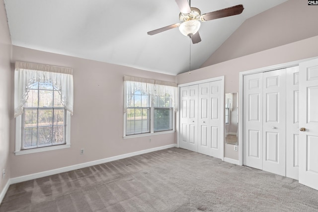 unfurnished bedroom with a ceiling fan, baseboards, carpet floors, vaulted ceiling, and multiple closets