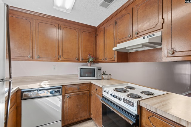 kitchen with visible vents, under cabinet range hood, light countertops, brown cabinets, and white appliances