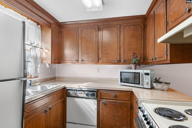 kitchen featuring under cabinet range hood, brown cabinets, stainless steel appliances, and light countertops