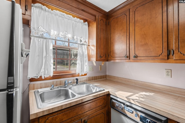 kitchen with a sink, freestanding refrigerator, brown cabinetry, light countertops, and dishwasher