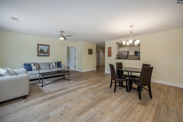 dining space with light wood-style flooring, ceiling fan with notable chandelier, and baseboards