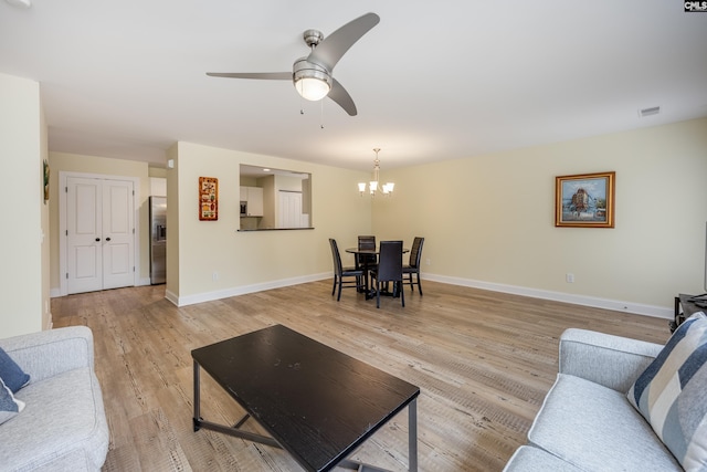 living room with visible vents, ceiling fan with notable chandelier, baseboards, and light wood-style floors