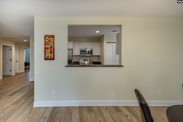 kitchen featuring white cabinets, wood finished floors, baseboards, and stainless steel appliances