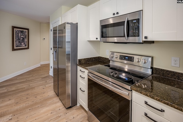 kitchen with stainless steel appliances, dark stone counters, light wood-style floors, white cabinets, and baseboards