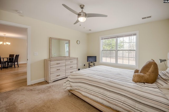 bedroom with light carpet, visible vents, ceiling fan with notable chandelier, and baseboards