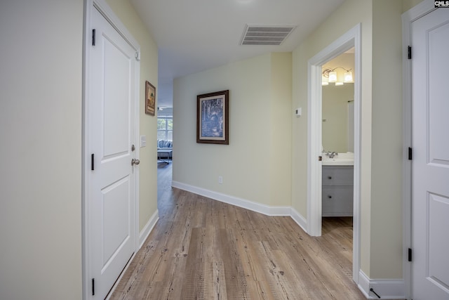 corridor featuring a sink, visible vents, baseboards, and light wood-style flooring