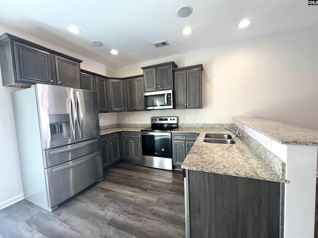 kitchen with recessed lighting, appliances with stainless steel finishes, a peninsula, dark wood-style floors, and a sink