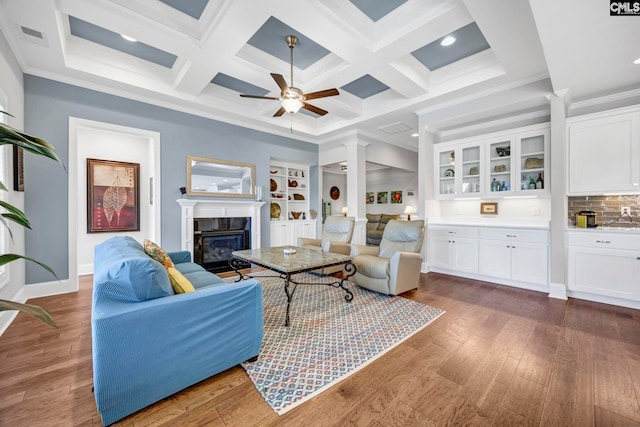 living area featuring a ceiling fan, coffered ceiling, a premium fireplace, ornamental molding, and wood-type flooring