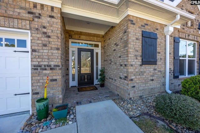 view of exterior entry with a garage and brick siding