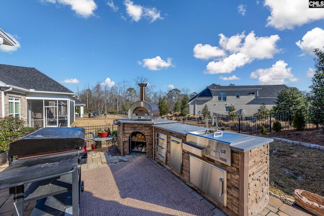 view of patio with fence, area for grilling, an outdoor kitchen, and a sunroom