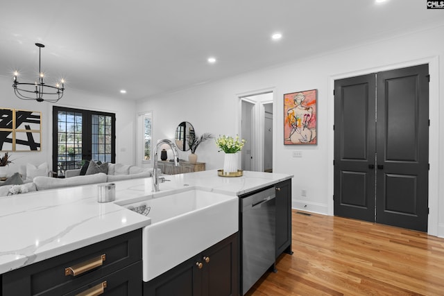 kitchen with dark cabinets, open floor plan, light wood-style flooring, stainless steel dishwasher, and a sink