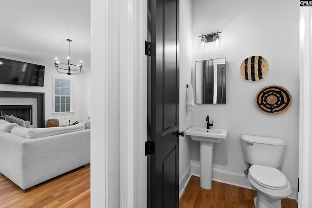 half bath with wood finished floors, baseboards, toilet, a fireplace, and a notable chandelier