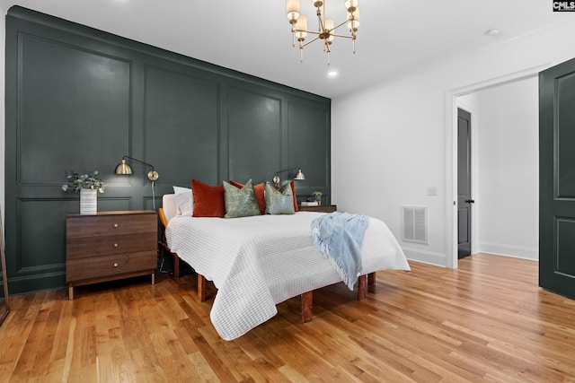 bedroom with light wood-type flooring, visible vents, a chandelier, and a decorative wall