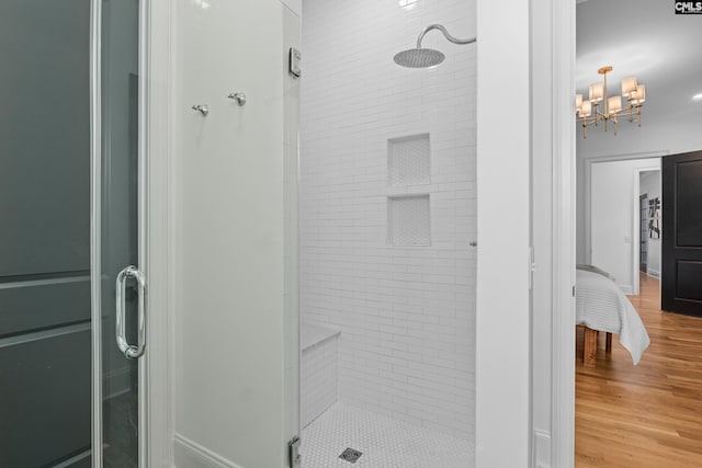 ensuite bathroom with a notable chandelier, a stall shower, ensuite bath, and wood finished floors