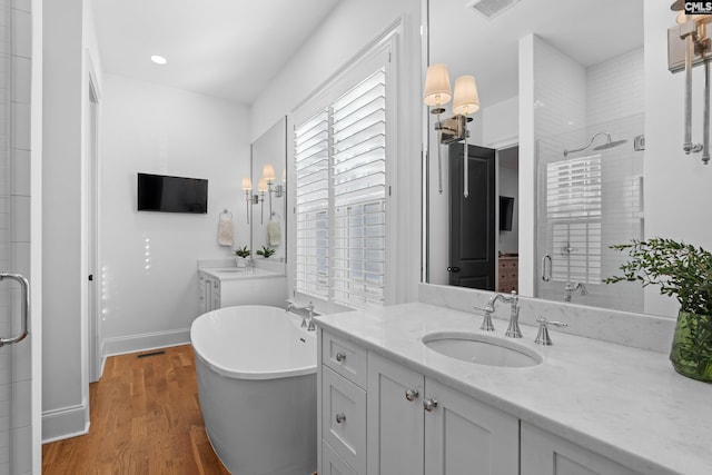 full bathroom featuring a shower stall, a freestanding bath, wood finished floors, and a sink