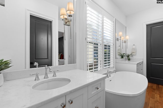 full bath with vanity, a freestanding tub, and wood finished floors