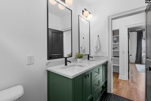 bathroom with double vanity, toilet, wood finished floors, and a sink