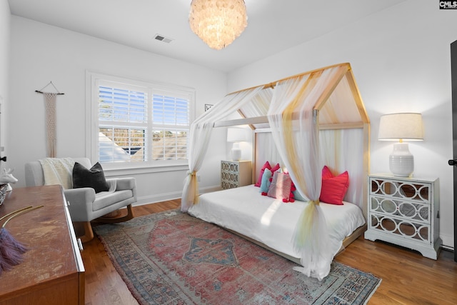 bedroom featuring baseboards, wood finished floors, visible vents, and a chandelier