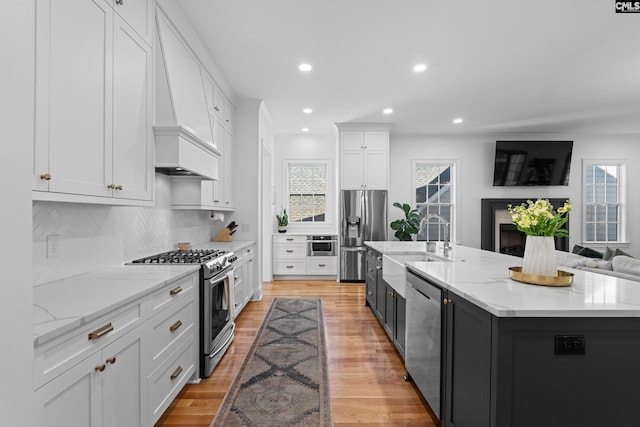 kitchen with custom exhaust hood, a sink, stainless steel appliances, white cabinetry, and open floor plan