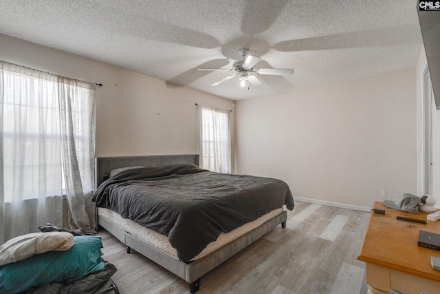 bedroom featuring light wood finished floors, a textured ceiling, baseboards, and a ceiling fan