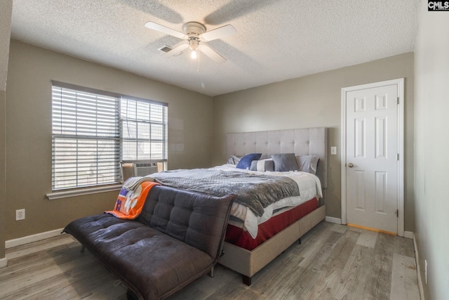 bedroom with light wood-style flooring, cooling unit, a textured ceiling, and baseboards