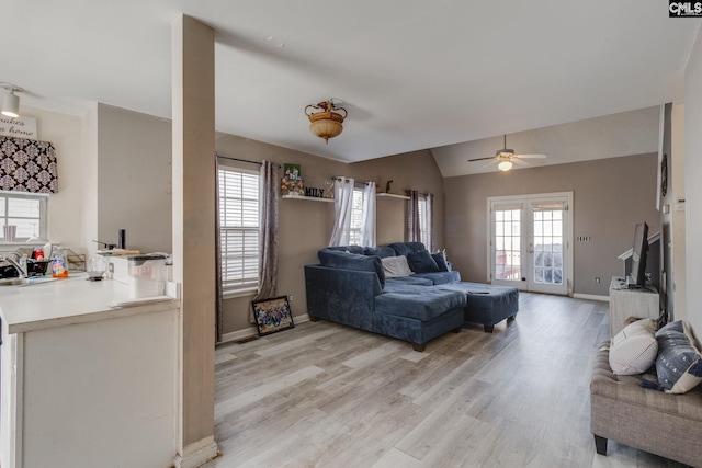 living area featuring lofted ceiling, baseboards, light wood finished floors, and ceiling fan