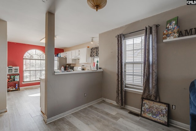 interior space with baseboards, light wood finished floors, freestanding refrigerator, under cabinet range hood, and white cabinetry