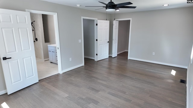 unfurnished bedroom featuring visible vents, baseboards, ensuite bathroom, wood finished floors, and a ceiling fan