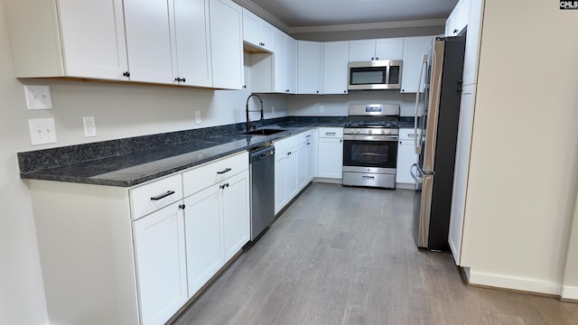 kitchen with crown molding, appliances with stainless steel finishes, light wood-style floors, white cabinetry, and a sink