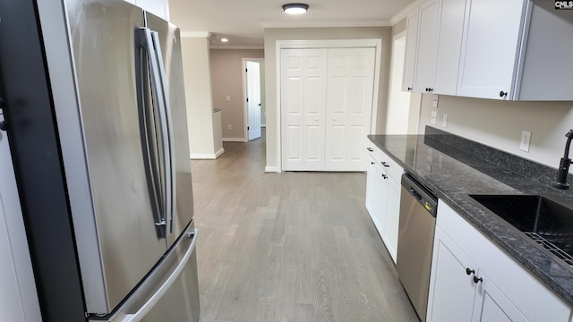 kitchen featuring dark stone counters, light wood-type flooring, ornamental molding, appliances with stainless steel finishes, and white cabinetry