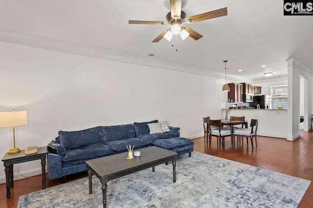 living area featuring wood finished floors, baseboards, decorative columns, ceiling fan, and crown molding