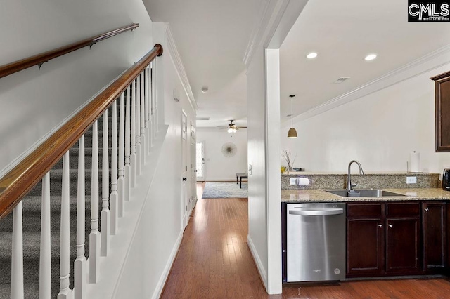 kitchen featuring dark wood-type flooring, ornamental molding, light stone counters, stainless steel dishwasher, and a sink