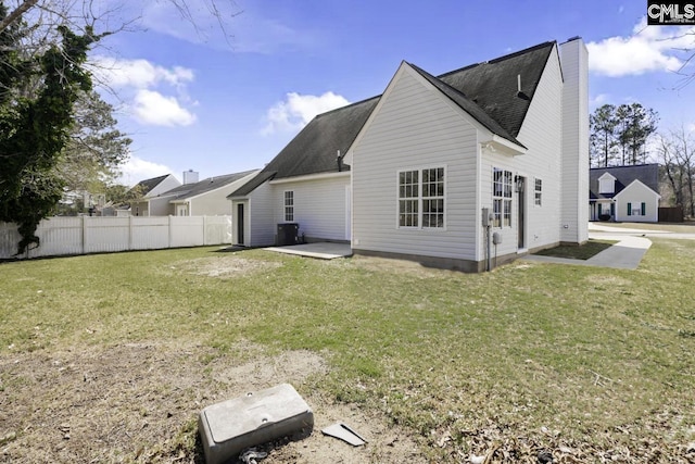 rear view of house featuring a yard, fence, a chimney, and a shingled roof