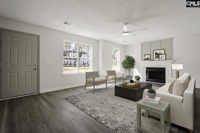 living room featuring visible vents, baseboards, ceiling fan, dark wood-style floors, and a textured ceiling