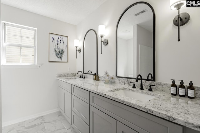 full bathroom with visible vents, marble finish floor, a textured ceiling, and a sink