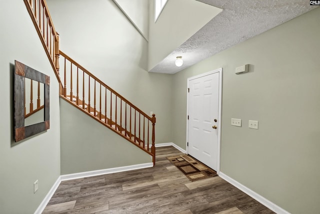 entryway featuring a textured ceiling, stairs, baseboards, and wood finished floors