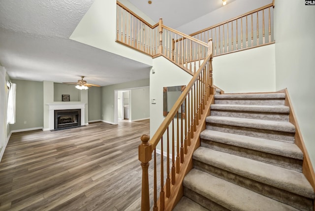 stairs with a fireplace, wood finished floors, baseboards, and ceiling fan