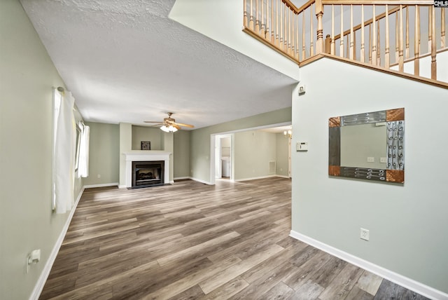 unfurnished living room featuring baseboards, a fireplace with flush hearth, wood finished floors, and a ceiling fan