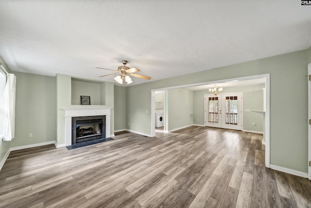 unfurnished living room featuring baseboards, a fireplace with flush hearth, ceiling fan with notable chandelier, wood finished floors, and washer / clothes dryer