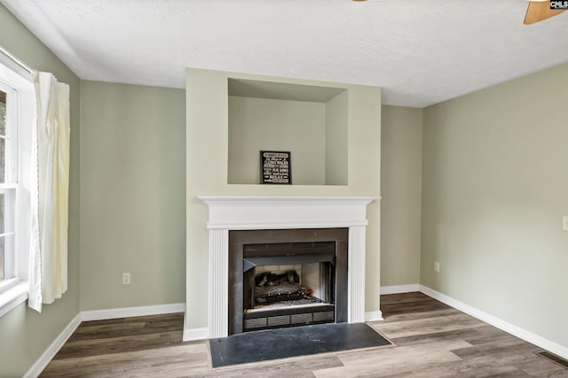 unfurnished living room with a fireplace with flush hearth, a textured ceiling, baseboards, and wood finished floors